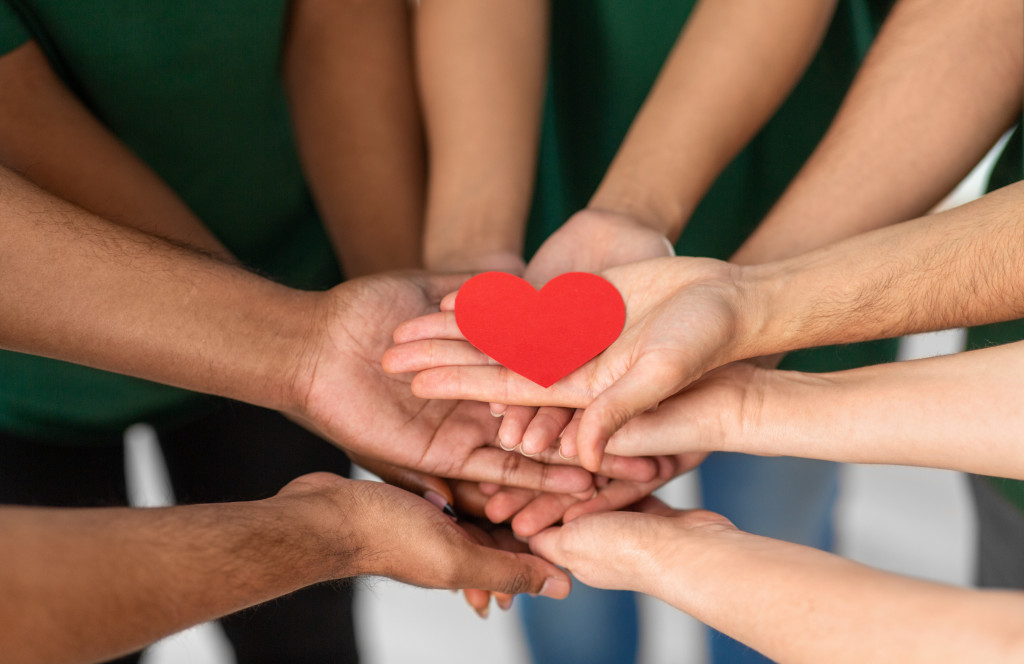 volunteers wearing green shirts holding together a paper red heart